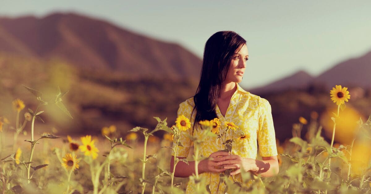 Woman solopreneur in sunflower field mountainous background serene yet longing for energy balance and recovery from burnout